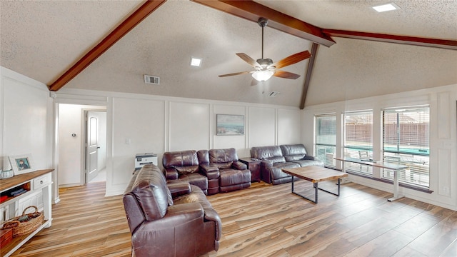 living room featuring light wood finished floors, visible vents, lofted ceiling with beams, a textured ceiling, and a decorative wall