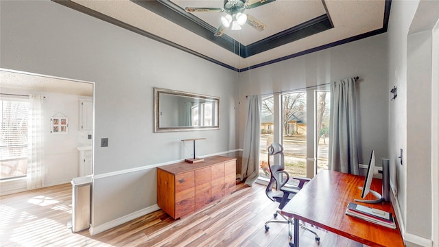 office featuring light wood finished floors, a raised ceiling, ornamental molding, ceiling fan, and baseboards