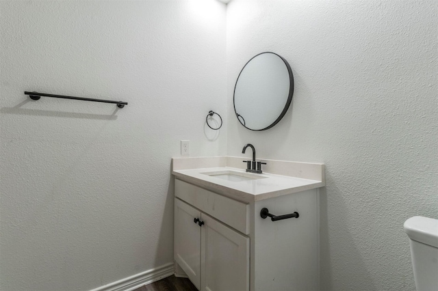 half bath with a textured wall, vanity, toilet, and wood finished floors