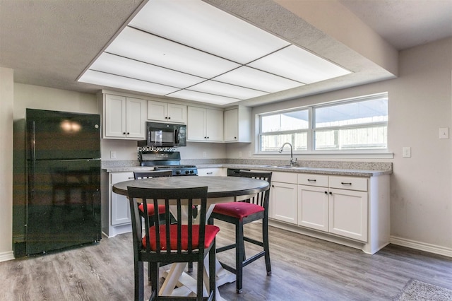 kitchen featuring baseboards, white cabinets, light wood-style floors, light countertops, and black appliances