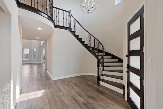 foyer entrance with a notable chandelier, dark wood finished floors, a towering ceiling, and baseboards