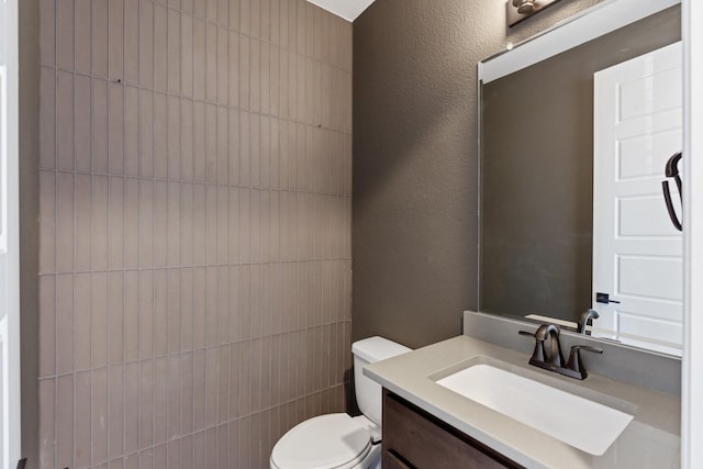 bathroom with toilet, a textured wall, and vanity