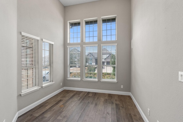 spare room featuring a towering ceiling, baseboards, and dark wood finished floors