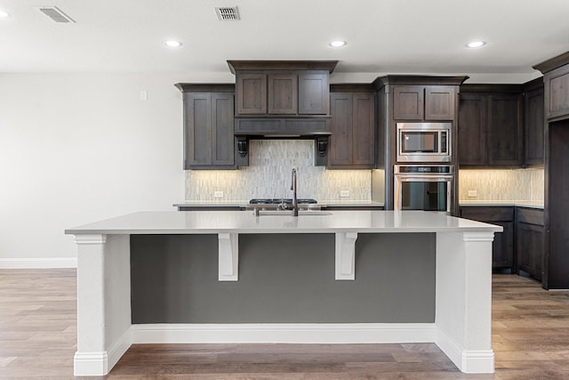 kitchen with appliances with stainless steel finishes, light countertops, visible vents, and a center island with sink