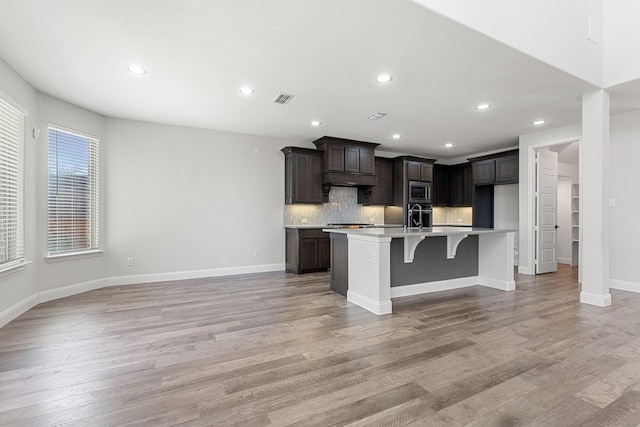 kitchen featuring visible vents, a kitchen island with sink, light countertops, light wood-style floors, and backsplash