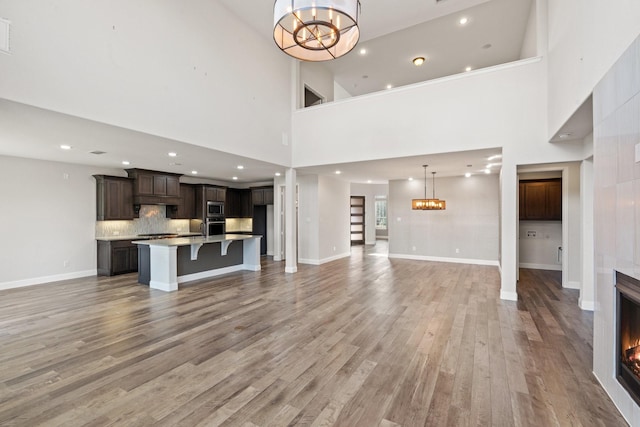 unfurnished living room with a chandelier, wood finished floors, baseboards, stairs, and a lit fireplace