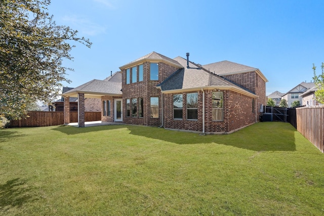 rear view of property with brick siding, a shingled roof, a lawn, a patio area, and a fenced backyard