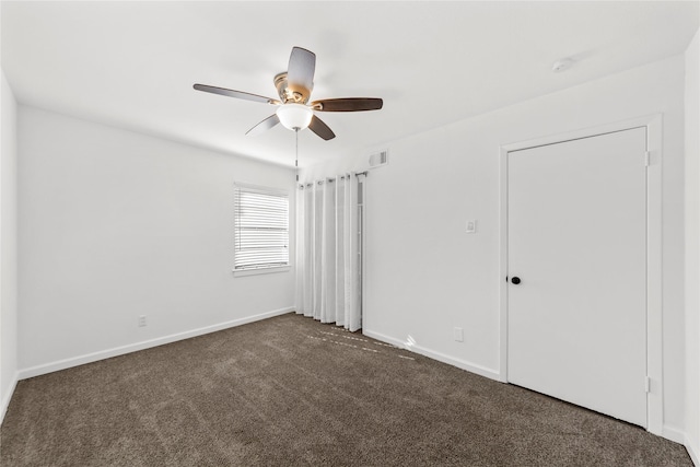 unfurnished room with ceiling fan, dark colored carpet, visible vents, and baseboards