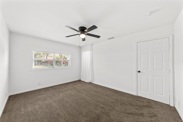 empty room with dark colored carpet, a ceiling fan, visible vents, and baseboards