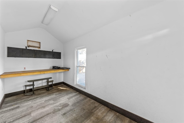 office space featuring vaulted ceiling, built in desk, baseboards, and wood finished floors