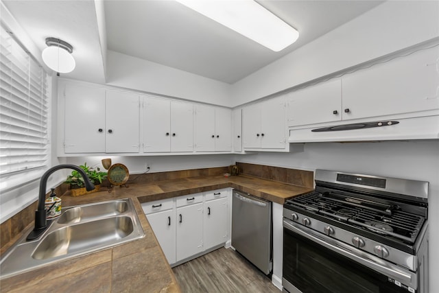 kitchen featuring under cabinet range hood, stainless steel appliances, a sink, white cabinets, and dark countertops