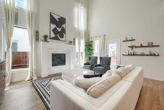 living area featuring light wood-type flooring, a glass covered fireplace, baseboards, and a high ceiling