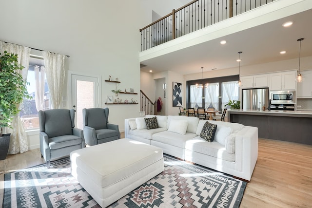 living area featuring recessed lighting, light wood-style flooring, a high ceiling, and stairs