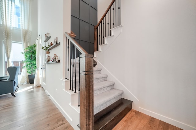 staircase with a towering ceiling, baseboards, and wood finished floors