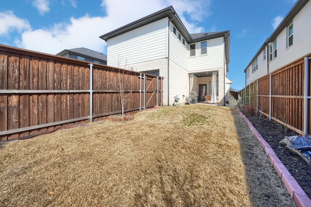rear view of house featuring a fenced backyard, a lawn, and brick siding