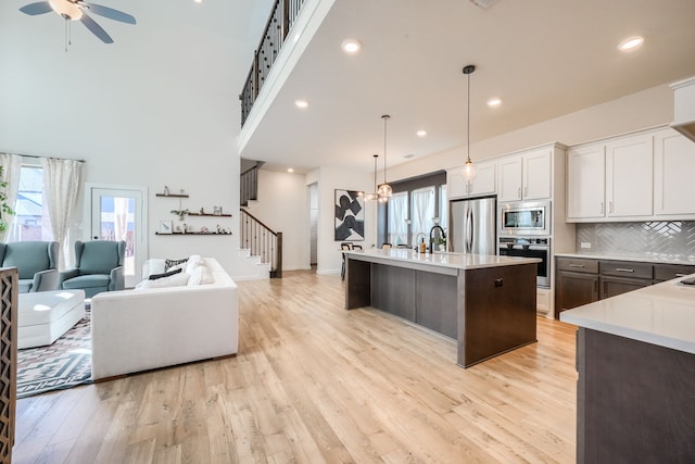 kitchen featuring decorative light fixtures, stainless steel appliances, light countertops, open floor plan, and white cabinetry