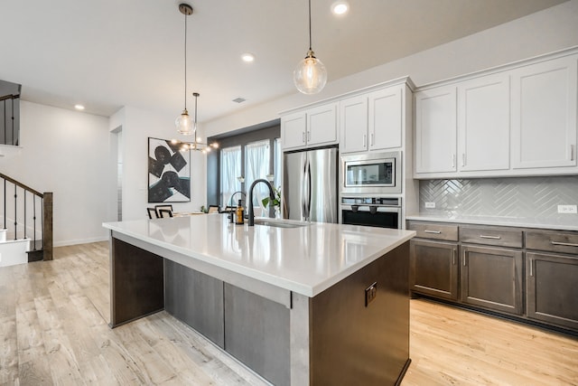 kitchen featuring stainless steel appliances, light countertops, a center island with sink, and decorative light fixtures