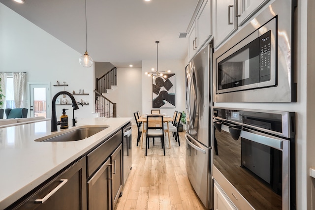 kitchen with stainless steel appliances, light countertops, hanging light fixtures, a sink, and light wood-type flooring