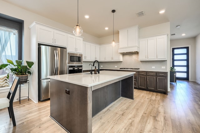 kitchen with a center island with sink, stainless steel appliances, light countertops, white cabinetry, and a sink