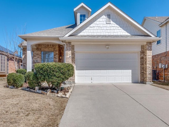 view of front of house with an attached garage, roof with shingles, concrete driveway, and brick siding