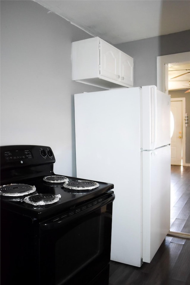 kitchen featuring dark wood-type flooring, freestanding refrigerator, black electric range oven, and white cabinetry