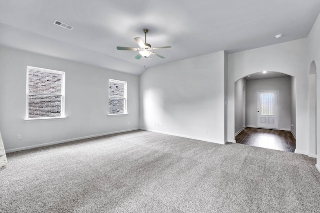 unfurnished room with baseboards, visible vents, arched walkways, a ceiling fan, and dark colored carpet