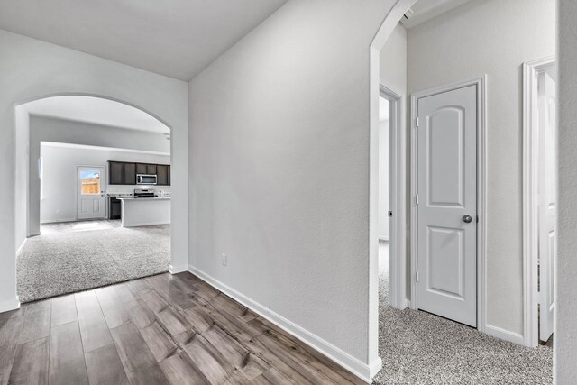 hall featuring arched walkways, baseboards, light carpet, and light wood finished floors