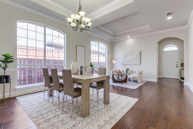 dining room with arched walkways, a raised ceiling, hardwood / wood-style floors, crown molding, and a notable chandelier