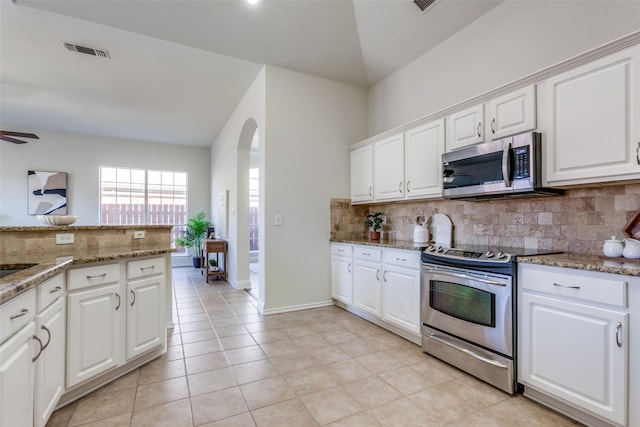 kitchen featuring arched walkways, light stone counters, appliances with stainless steel finishes, and white cabinetry