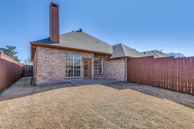 rear view of house with roof with shingles, brick siding, a chimney, and a fenced backyard