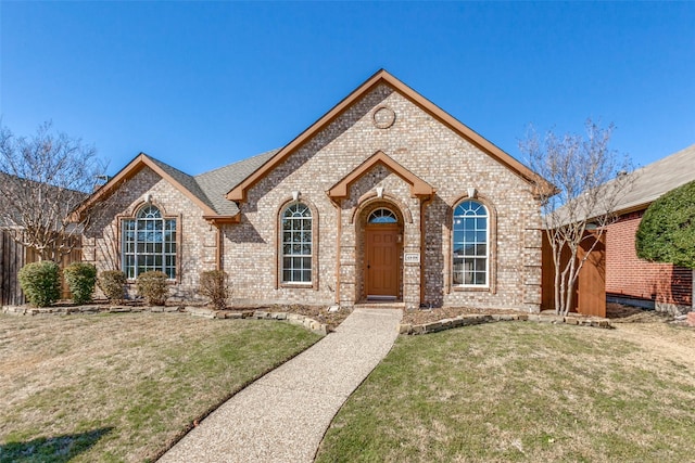 french provincial home featuring brick siding, a front yard, and fence