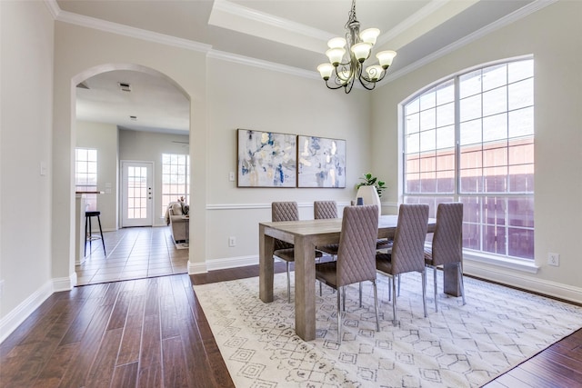 dining room featuring arched walkways, a tray ceiling, and wood finished floors