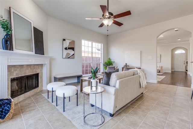 living area with arched walkways, light tile patterned floors, ceiling fan, and a tile fireplace