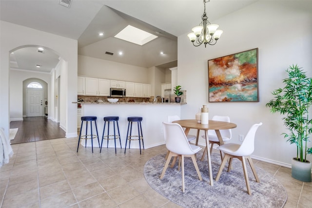 dining space featuring arched walkways, light tile patterned floors, visible vents, vaulted ceiling, and baseboards