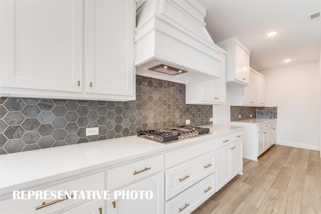 kitchen with white cabinets, custom range hood, light countertops, backsplash, and stainless steel gas stovetop