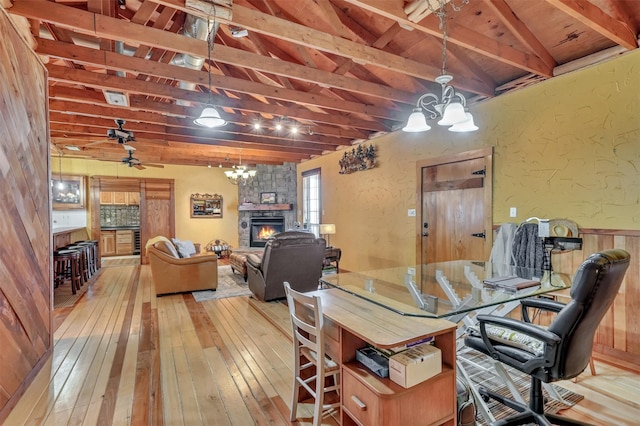 dining space featuring vaulted ceiling with beams, wood-type flooring, a chandelier, and a stone fireplace