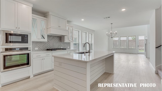 kitchen with decorative light fixtures, stainless steel appliances, light countertops, a kitchen island with sink, and a sink