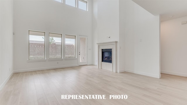 unfurnished living room with a glass covered fireplace, baseboards, a high ceiling, and light wood finished floors