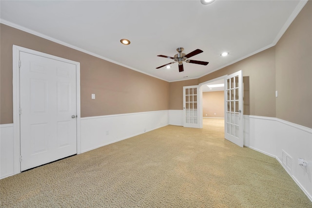 unfurnished room featuring french doors, light colored carpet, ornamental molding, wainscoting, and ceiling fan