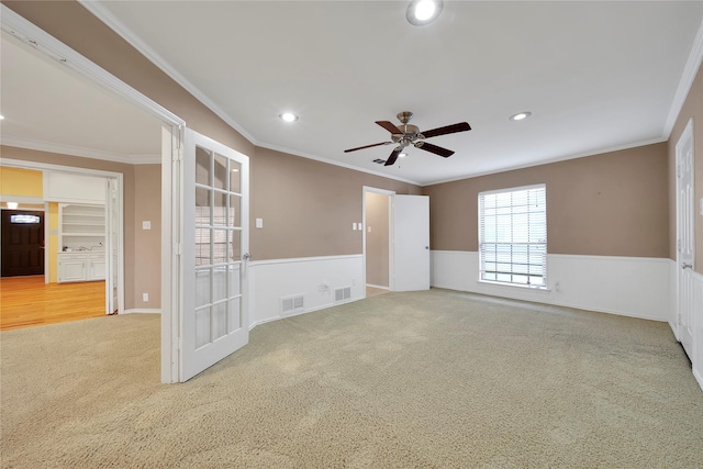 carpeted empty room with a wainscoted wall, ornamental molding, and visible vents