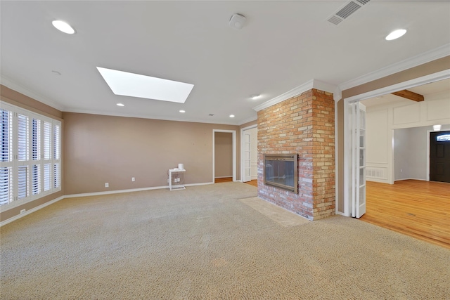 unfurnished living room with ornamental molding, a fireplace, a skylight, and light colored carpet