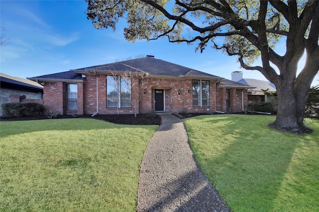 ranch-style home with roof with shingles, a front yard, a chimney, and brick siding