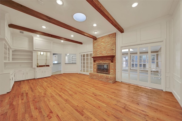 unfurnished living room featuring beam ceiling, a fireplace, recessed lighting, a decorative wall, and light wood-style floors