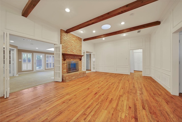 unfurnished living room featuring visible vents, light wood-style floors, a brick fireplace, a decorative wall, and beam ceiling