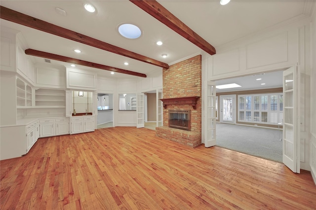 unfurnished living room with light wood-type flooring, a fireplace, a decorative wall, and beam ceiling