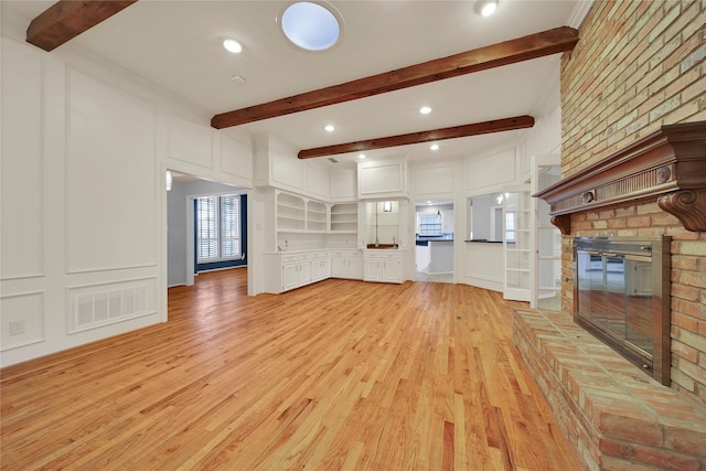 unfurnished living room with light wood finished floors, beam ceiling, visible vents, and a decorative wall