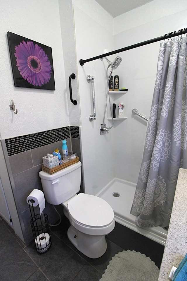 bathroom featuring toilet, tile patterned floors, tile walls, wainscoting, and a shower with curtain