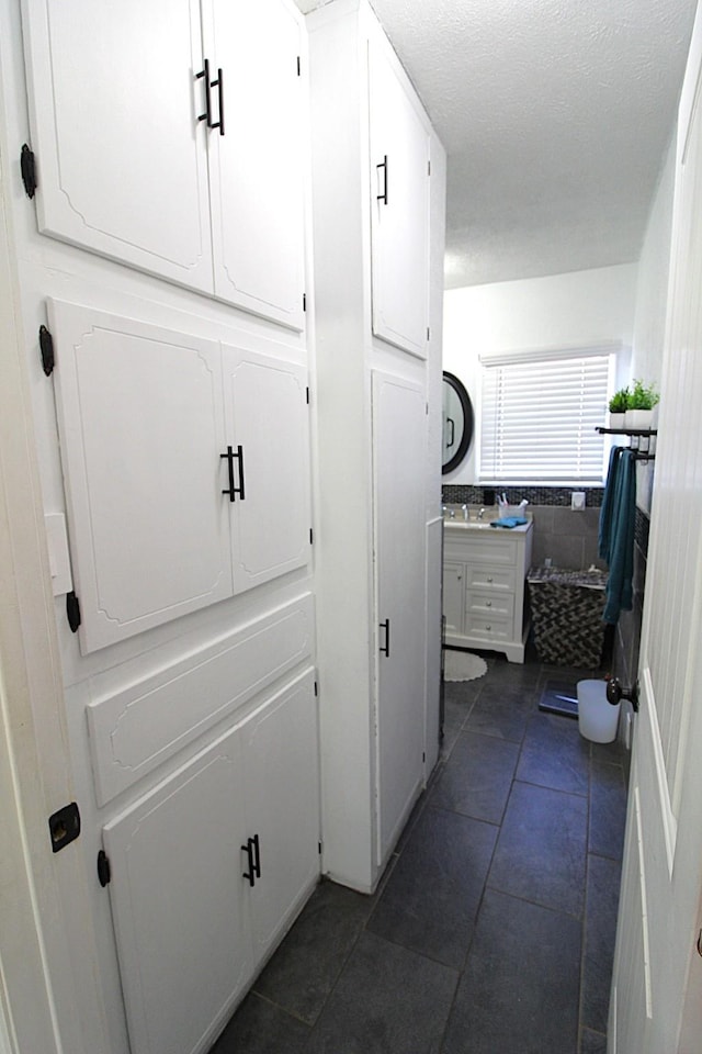 corridor with tile walls, dark tile patterned flooring, wainscoting, a textured ceiling, and a sink