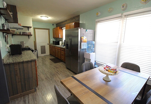 kitchen with open shelves, stainless steel refrigerator with ice dispenser, wood finished floors, and light stone countertops