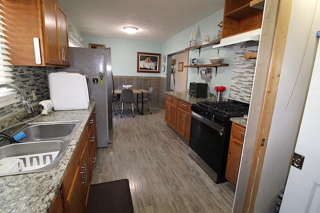 kitchen featuring brown cabinets, a wainscoted wall, open shelves, black gas stove, and a sink